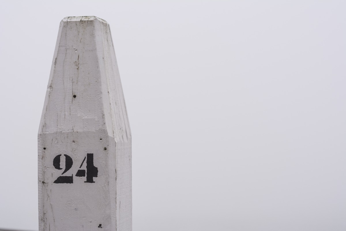 Weißer Holzpfosten mit der aufgemalten Zahl „24“ vor nebligem Hintergrund.