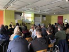 Schülerinnen und Schüler sitzen dicht gedrängt in einem Raum und verfolgen eine Präsentation an der Leinwand.