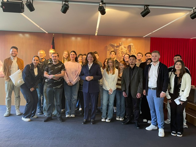 Gruppenfoto der Schülerinnen und Schüler mit der Verfassungsrichterin in einem holzvertäfelten Saal mit Bundesadler und Deutschlandflagge.