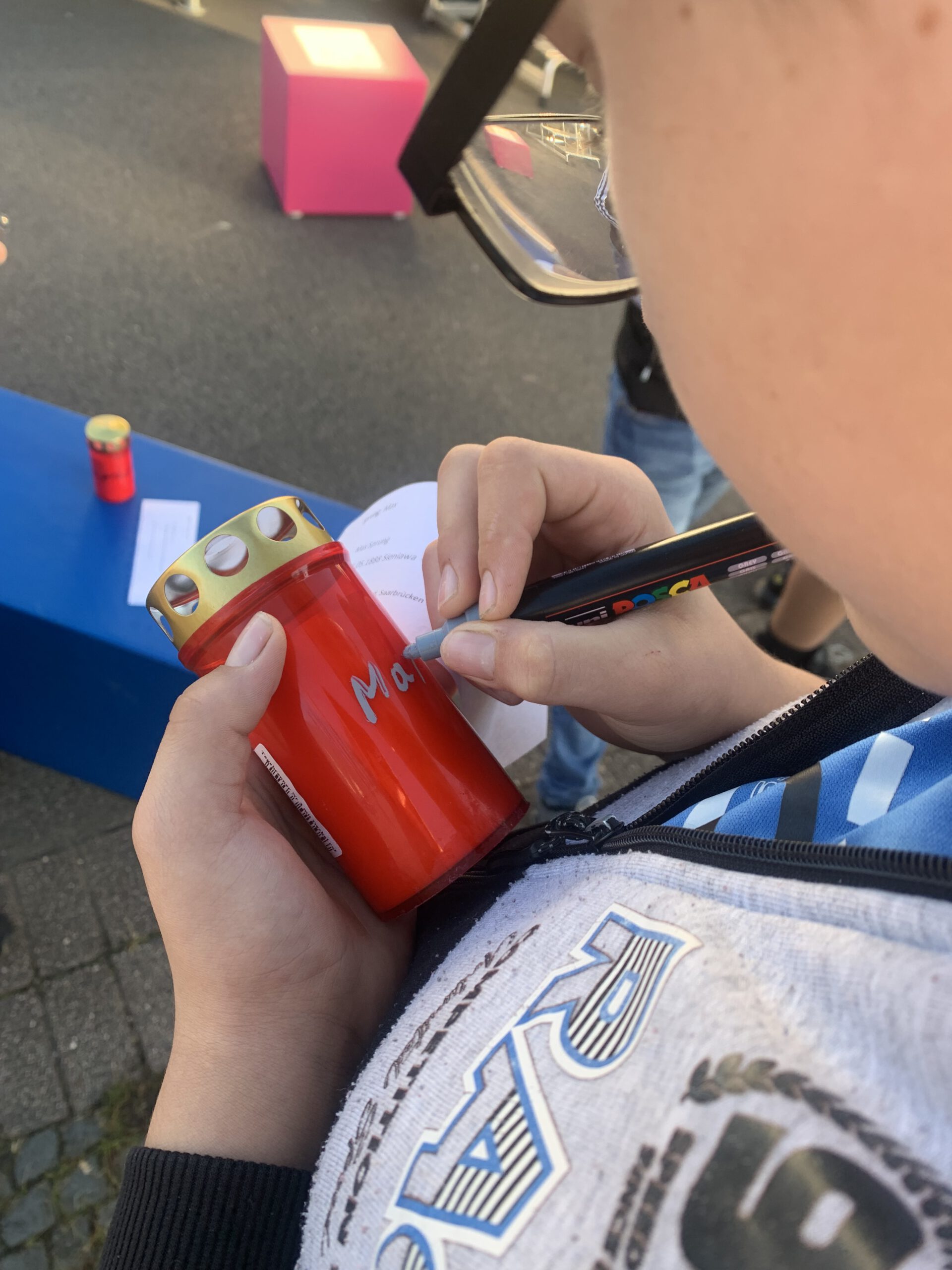 Eine Schülerin schreibt mit weißem Stift einen Namen auf eine rote Gedenkkerze.