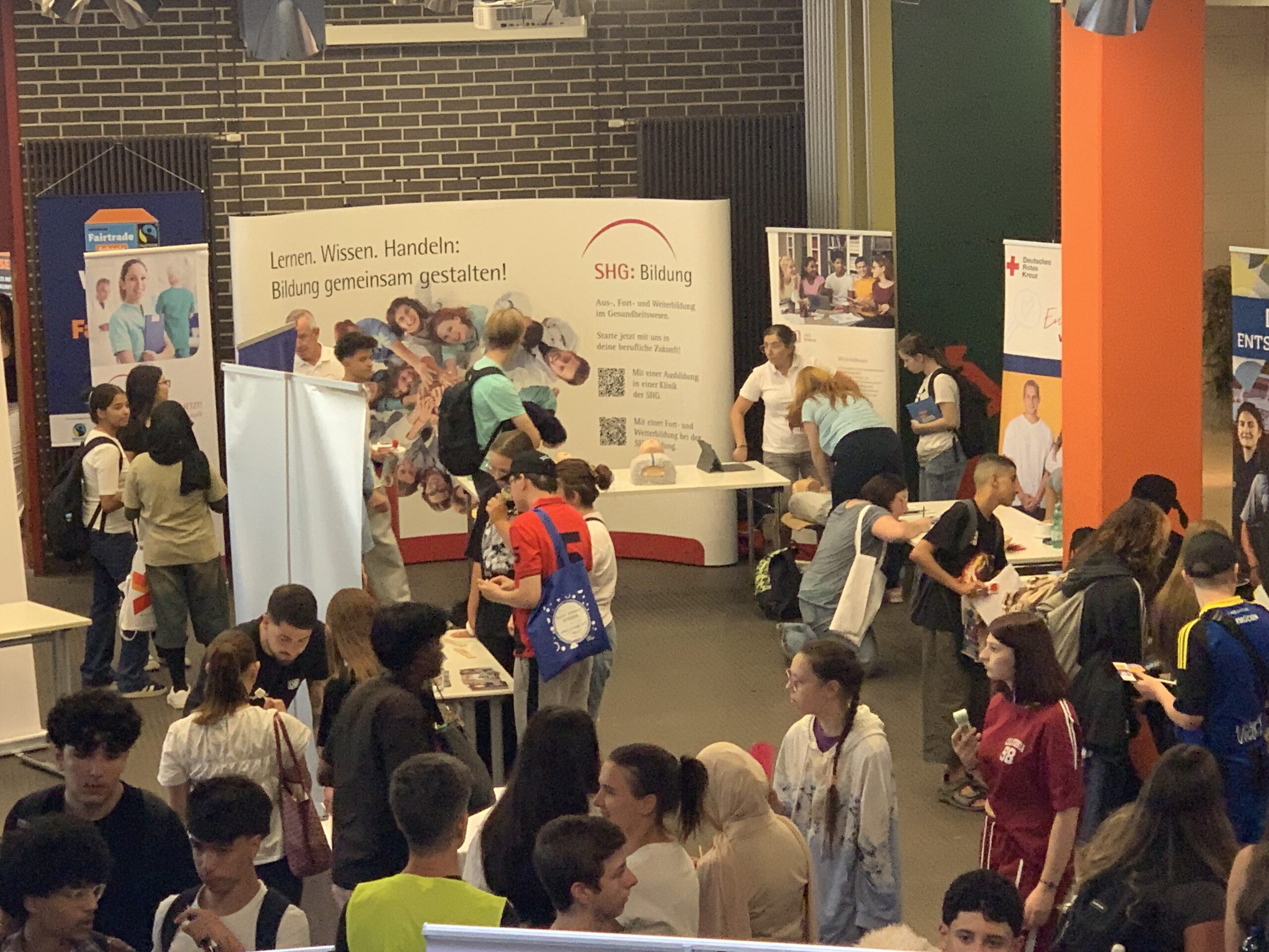 Überblick über die Berufsmesse in der Halle mit zahlreichen Ständen und Schülerinnen und Schülern